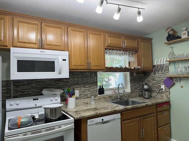 kitchen with white appliances, track lighting, sink, tasteful backsplash, and light stone counters