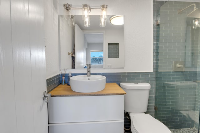 bathroom featuring tiled shower, vanity, tile walls, and toilet