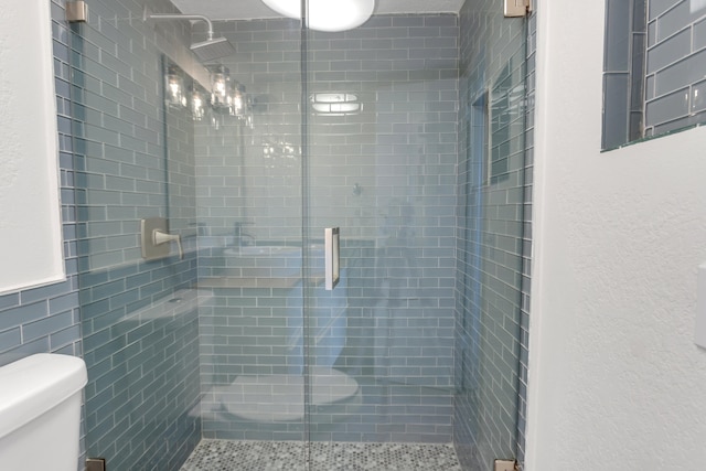 bathroom featuring a shower with door and toilet