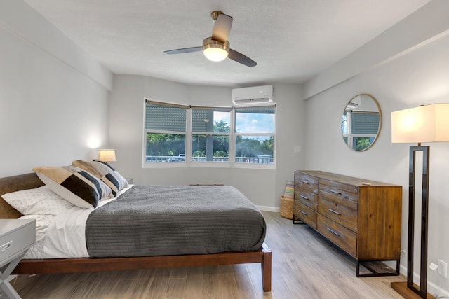 bedroom featuring ceiling fan, light wood-type flooring, and an AC wall unit