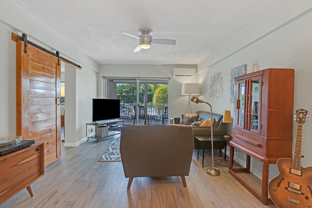 living room featuring ceiling fan, a barn door, light wood-type flooring, a textured ceiling, and a wall unit AC