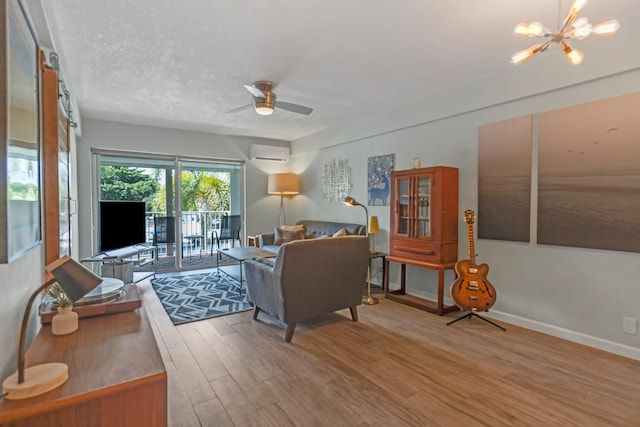 living room featuring a wall unit AC, hardwood / wood-style floors, a textured ceiling, and ceiling fan with notable chandelier