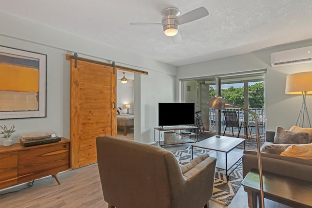 living room featuring an AC wall unit, light hardwood / wood-style flooring, ceiling fan, a barn door, and a textured ceiling