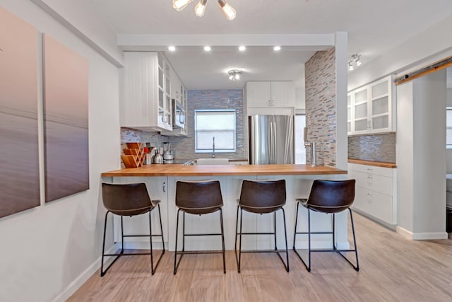 kitchen featuring stainless steel refrigerator, white cabinetry, wooden counters, light hardwood / wood-style floors, and a breakfast bar area