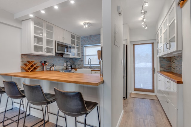 kitchen featuring butcher block counters, stainless steel appliances, tasteful backsplash, a breakfast bar area, and white cabinets