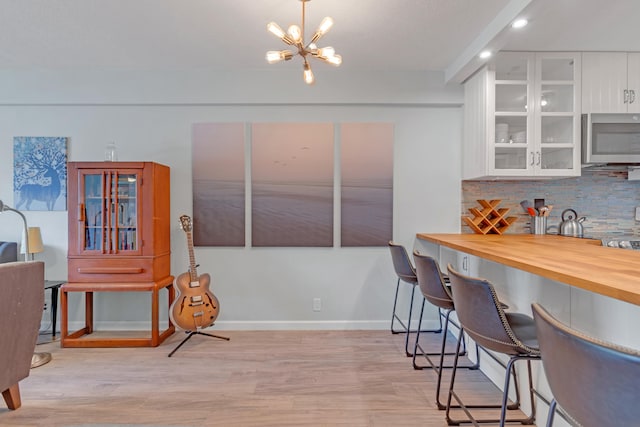 kitchen featuring wood counters, decorative backsplash, decorative light fixtures, light hardwood / wood-style flooring, and white cabinets