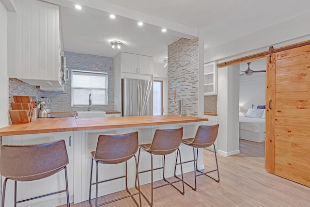 kitchen with butcher block countertops, a kitchen breakfast bar, stainless steel fridge, and a barn door