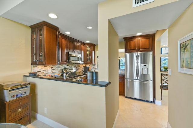 kitchen with stainless steel appliances, backsplash, kitchen peninsula, dark stone counters, and light tile patterned flooring