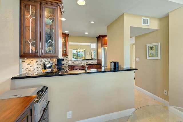 kitchen featuring a chandelier, kitchen peninsula, stainless steel refrigerator, and tasteful backsplash