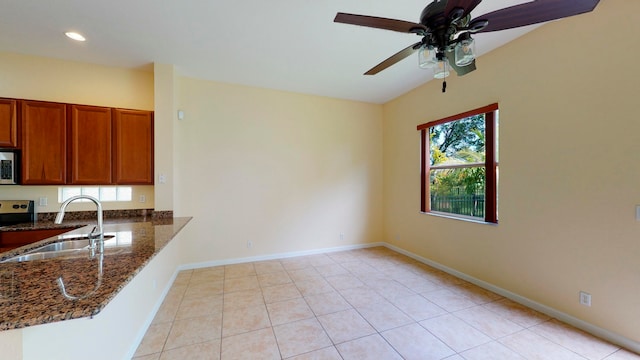 kitchen featuring kitchen peninsula, ceiling fan, sink, dark stone countertops, and light tile patterned flooring