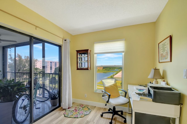 office space with a water view, a healthy amount of sunlight, a textured ceiling, and light hardwood / wood-style floors