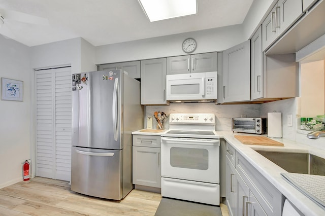 kitchen featuring gray cabinetry, white appliances, sink, light hardwood / wood-style flooring, and decorative backsplash