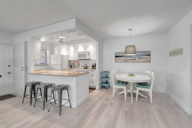 kitchen featuring kitchen peninsula, a kitchen breakfast bar, white appliances, light hardwood / wood-style flooring, and white cabinets