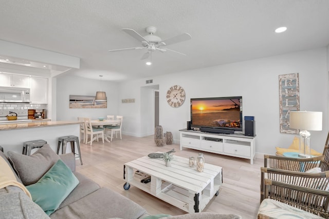 living room with a textured ceiling, light hardwood / wood-style floors, and ceiling fan