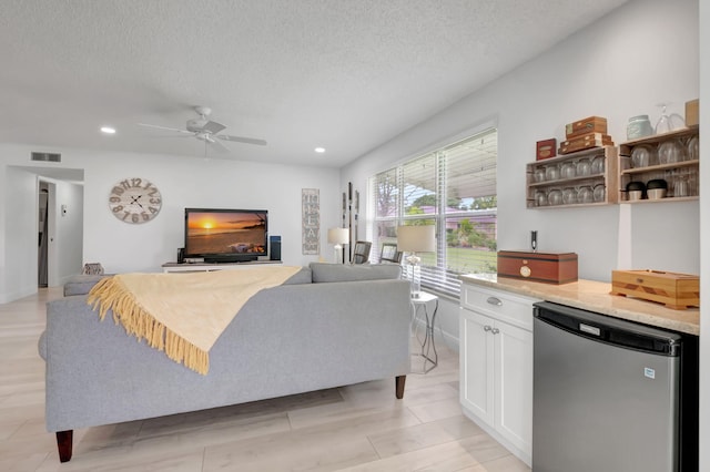 living room with ceiling fan, light hardwood / wood-style floors, and a textured ceiling