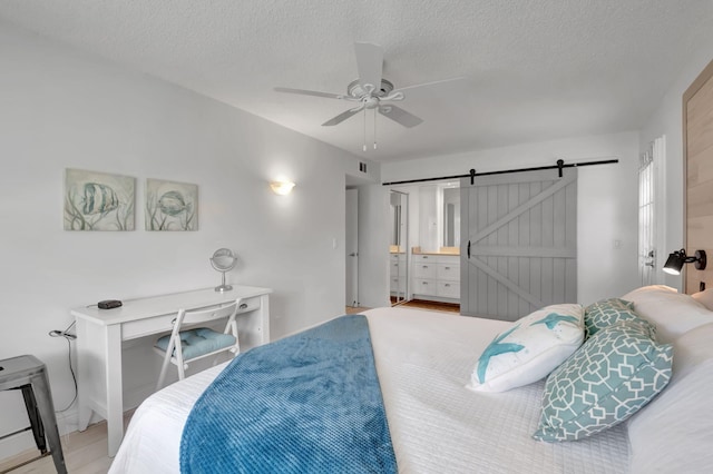 bedroom with ensuite bathroom, a textured ceiling, ceiling fan, a barn door, and hardwood / wood-style flooring