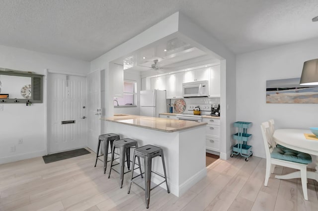 kitchen with white cabinetry, light wood-type flooring, white appliances, and a breakfast bar area