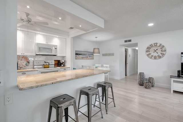 kitchen with a kitchen bar, white cabinetry, decorative light fixtures, and white appliances