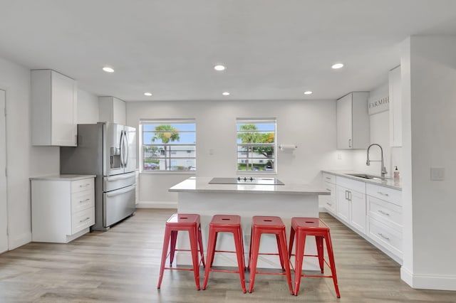 kitchen featuring white cabinets, sink, stainless steel fridge, light hardwood / wood-style floors, and a breakfast bar area