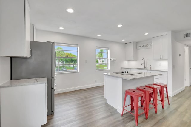 kitchen with sink, light wood-type flooring, a kitchen island, a kitchen bar, and white cabinetry