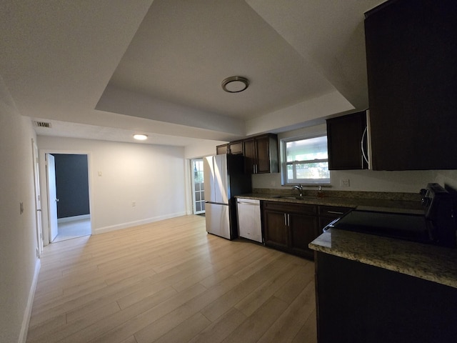 kitchen with a tray ceiling, sink, stainless steel appliances, and light hardwood / wood-style floors