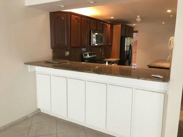 kitchen featuring light tile patterned flooring, dark stone countertops, kitchen peninsula, and appliances with stainless steel finishes