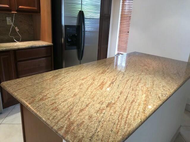 kitchen featuring light stone countertops, stainless steel refrigerator with ice dispenser, kitchen peninsula, and light tile patterned flooring