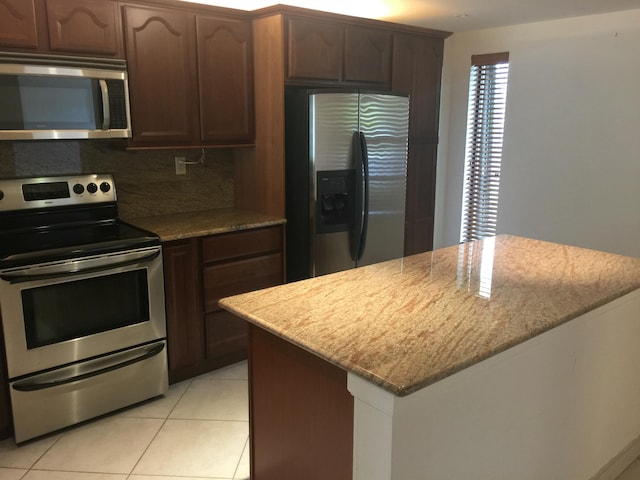 kitchen with backsplash, light stone countertops, light tile patterned floors, dark brown cabinetry, and stainless steel appliances