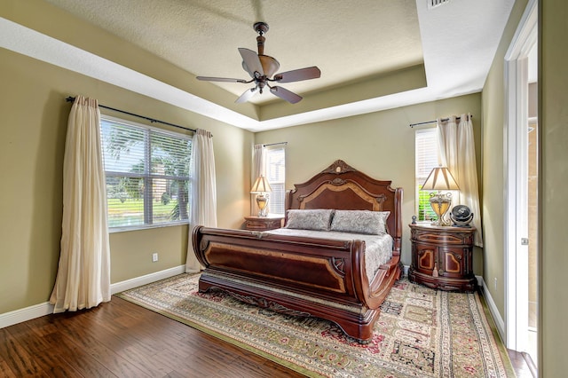 bedroom with ceiling fan, dark hardwood / wood-style flooring, multiple windows, and a tray ceiling