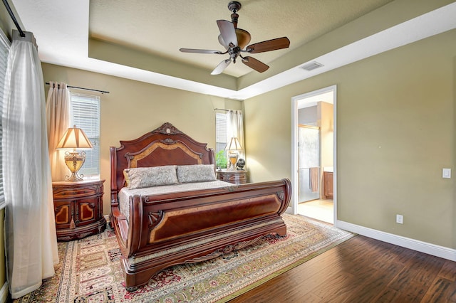 bedroom with ensuite bathroom, ceiling fan, a raised ceiling, and wood-type flooring