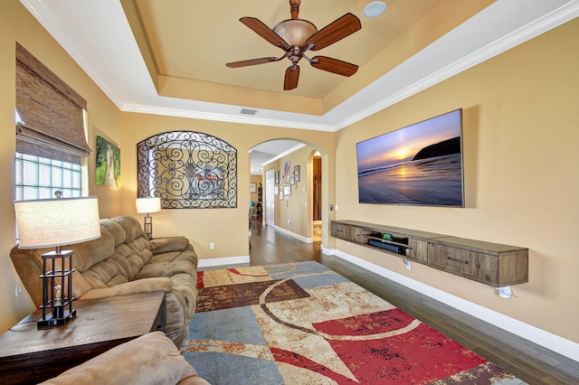 living room with a tray ceiling, ceiling fan, dark hardwood / wood-style floors, and ornamental molding