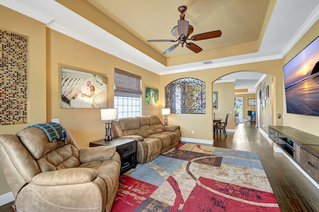 living room with a raised ceiling, dark hardwood / wood-style flooring, ceiling fan, and crown molding