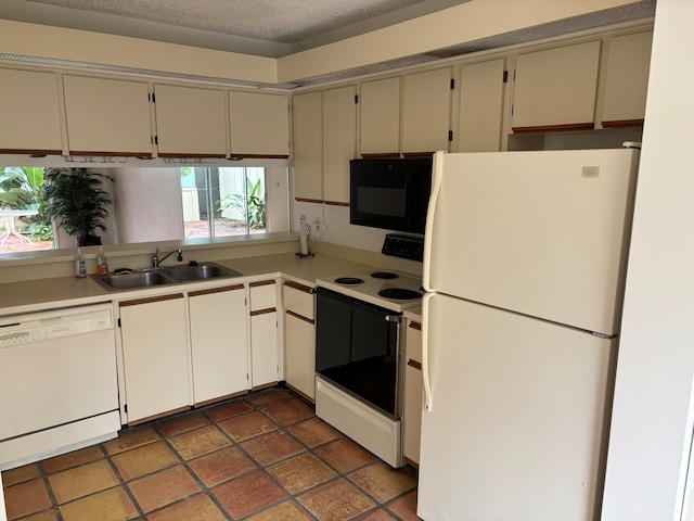 kitchen with white appliances, dark tile patterned flooring, sink, a textured ceiling, and cream cabinetry