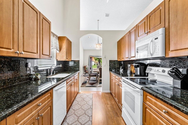 kitchen featuring white appliances, sink, hanging light fixtures, light wood-type flooring, and a textured ceiling