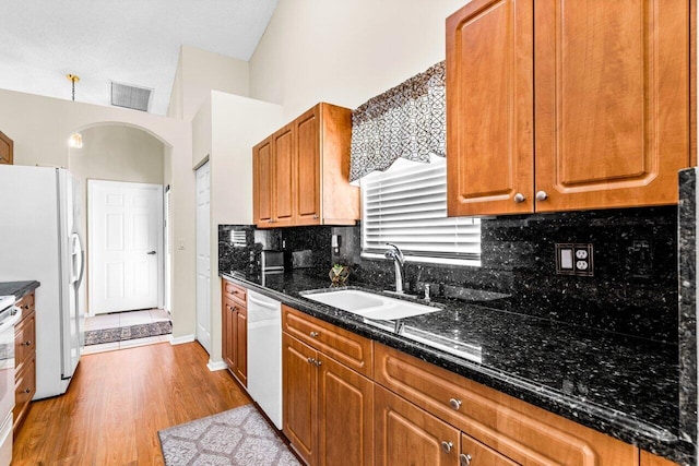 kitchen with white appliances, light hardwood / wood-style flooring, dark stone countertops, and sink