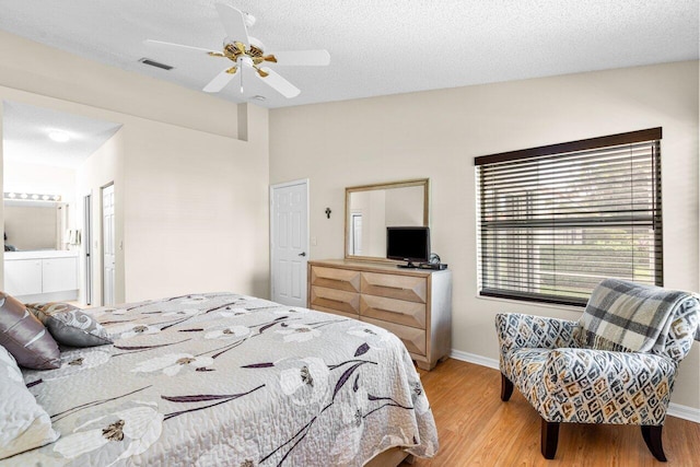 bedroom featuring a textured ceiling, light wood-type flooring, ceiling fan, and connected bathroom