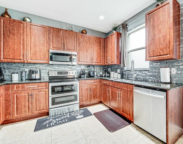 kitchen with decorative backsplash, stainless steel appliances, sink, dark stone countertops, and light tile patterned flooring