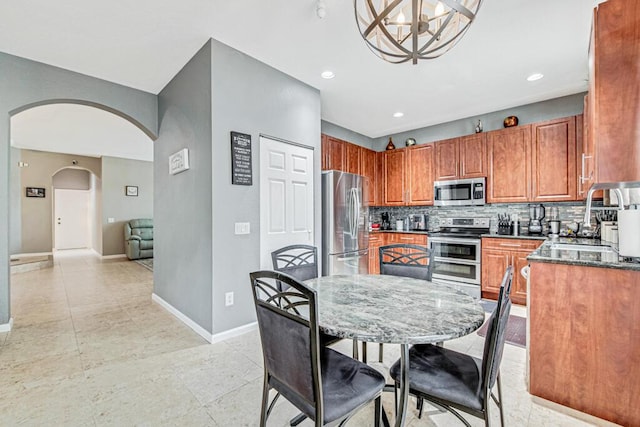 kitchen with decorative backsplash, stainless steel appliances, sink, dark stone countertops, and a chandelier