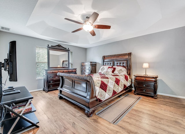 bedroom with ceiling fan, light wood-type flooring, and a tray ceiling