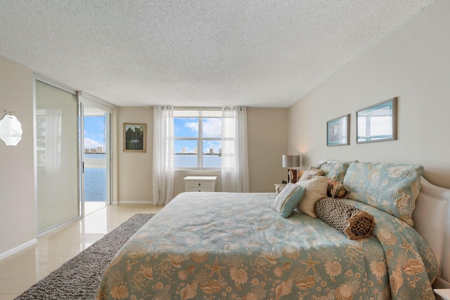 tiled bedroom featuring a textured ceiling, a water view, and expansive windows