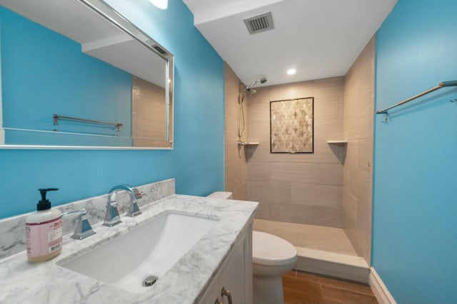 bathroom with hardwood / wood-style floors, vanity, toilet, and tiled shower