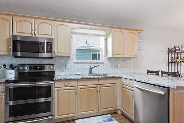 kitchen featuring kitchen peninsula, stainless steel appliances, light stone countertops, and sink