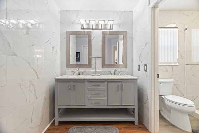 bathroom with vanity, a textured ceiling, wood-type flooring, tile walls, and toilet