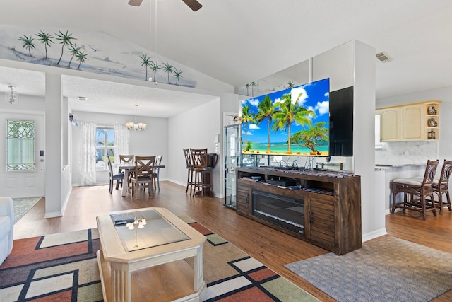 living room featuring wood-type flooring, ceiling fan with notable chandelier, a textured ceiling, and vaulted ceiling