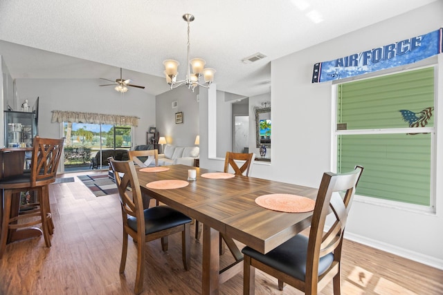 dining room with a textured ceiling, ceiling fan with notable chandelier, hardwood / wood-style flooring, and lofted ceiling