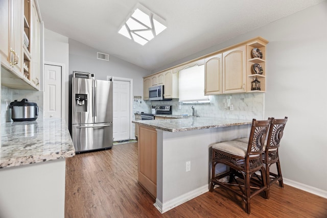 kitchen with light stone countertops, appliances with stainless steel finishes, dark wood-type flooring, and a breakfast bar area