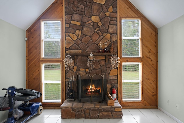 living room with wood walls, light tile patterned flooring, a stone fireplace, and high vaulted ceiling