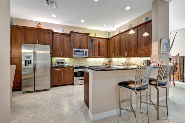 kitchen featuring pendant lighting, tasteful backsplash, light tile patterned flooring, a kitchen bar, and stainless steel appliances