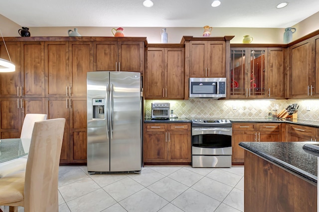 kitchen featuring decorative backsplash, light tile patterned flooring, stainless steel appliances, and dark stone counters