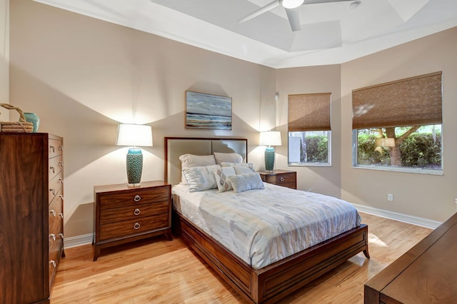 bedroom with ceiling fan, light wood-type flooring, and a tray ceiling